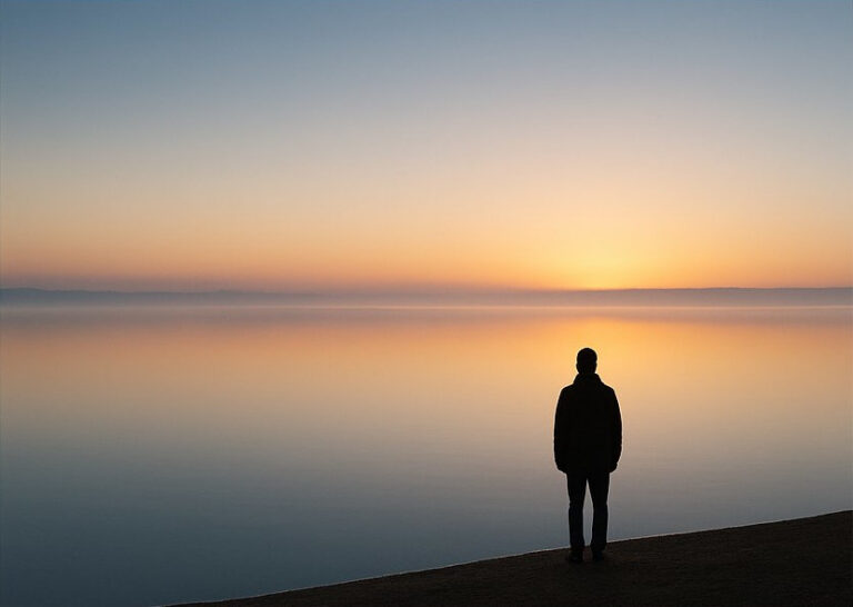 silhouette of someone standing by the sea at sunrise